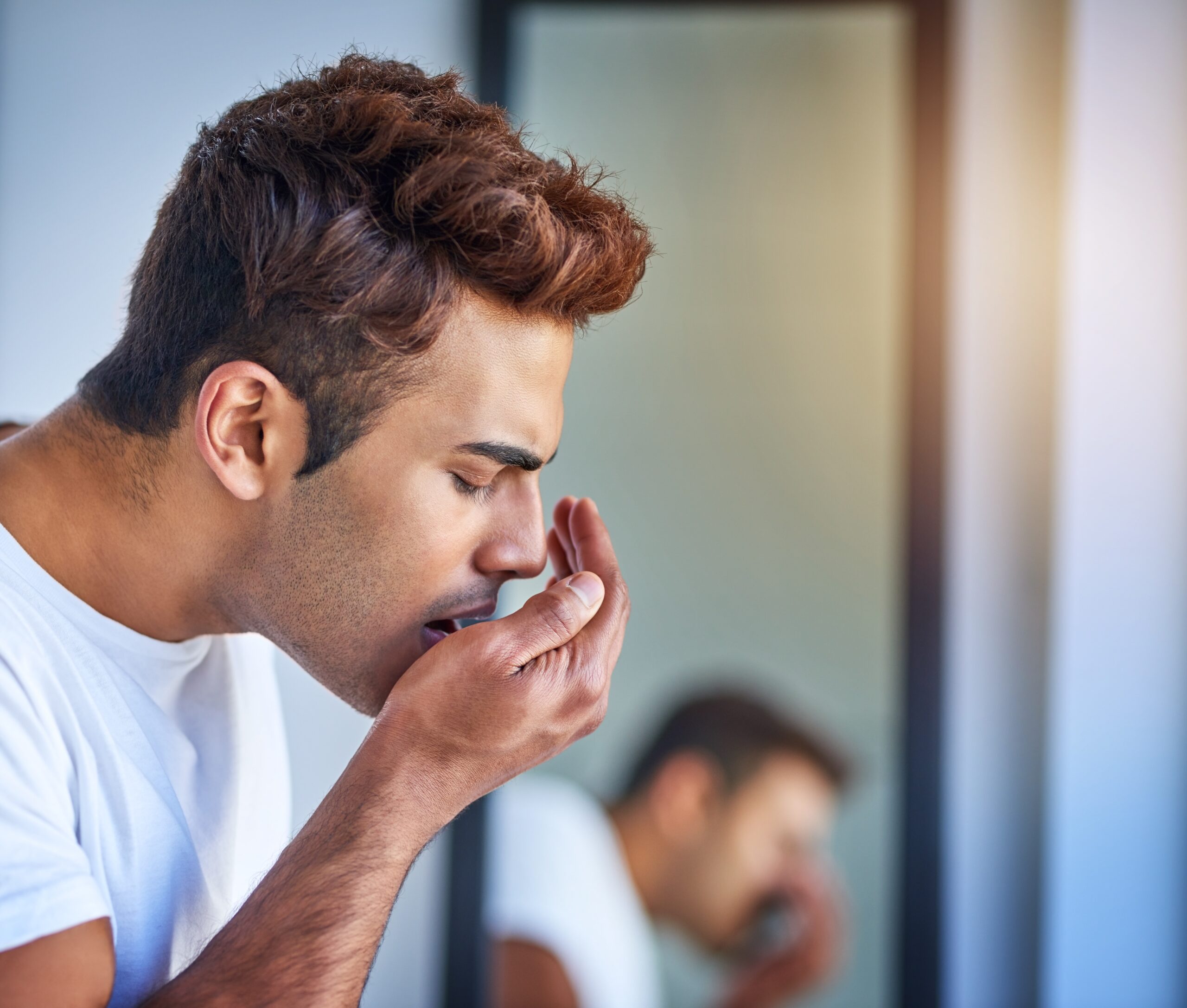 young man blowing into his hand checking his breath