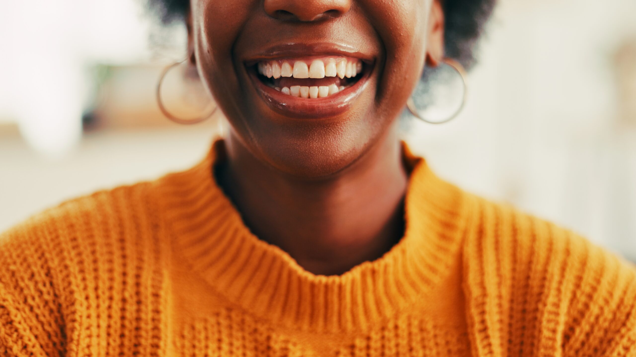 closeup of a woman smiling in a orange sweater, perfect white teeth